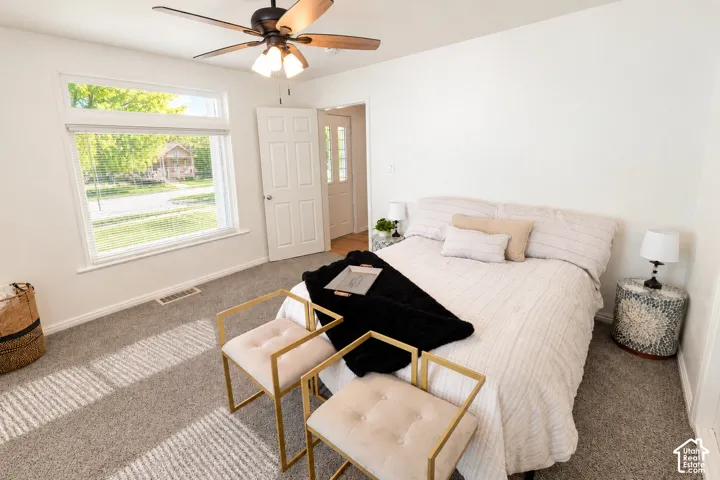 Neutral-toned carpeting, large picture window with natural light, multi-panel interior doors, and a ceiling fan with integrated lighting