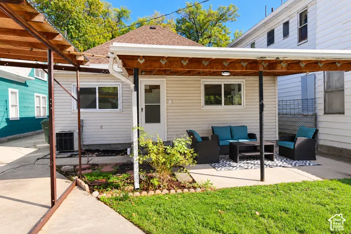 Exterior features include a covered patio with a wooden structural frame, light-toned horizontal siding, and a concrete patio surface