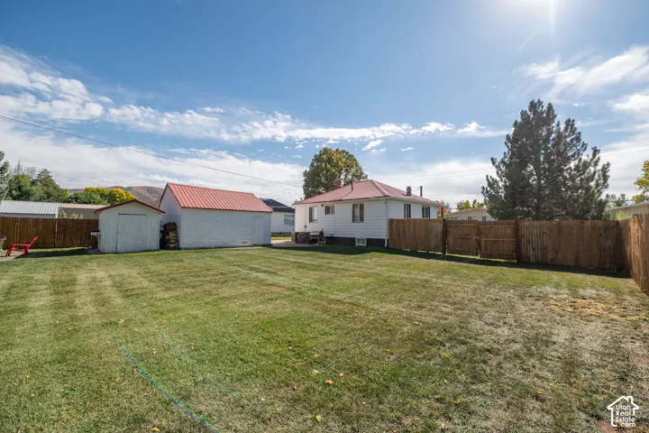 Expansive lawn area, wood privacy fencing, detached garage with red metal roof, additional storage shed, and mature trees