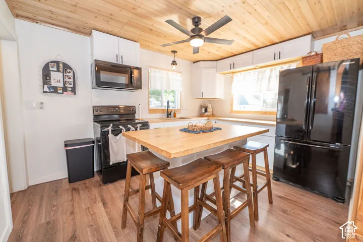 Wood-finish flooring, wood plank ceiling, white cabinetry with black hardware, black appliances, and a built-in island with seating