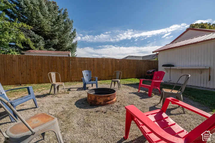 Gravel patio area featuring a built-in fire pit, privacy fencing, and an outbuilding with a metal roof