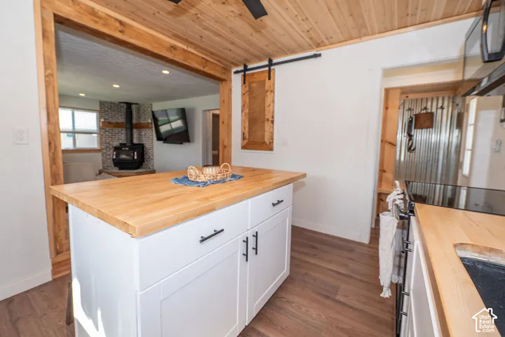 Wood-finish flooring with a wood ceiling, wood island countertop, and white cabinetry