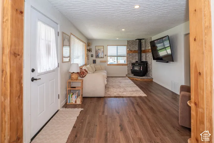 Wood-finish flooring, recessed ceiling lighting, a wood-burning stove with a brick surround, and multiple windows with blinds