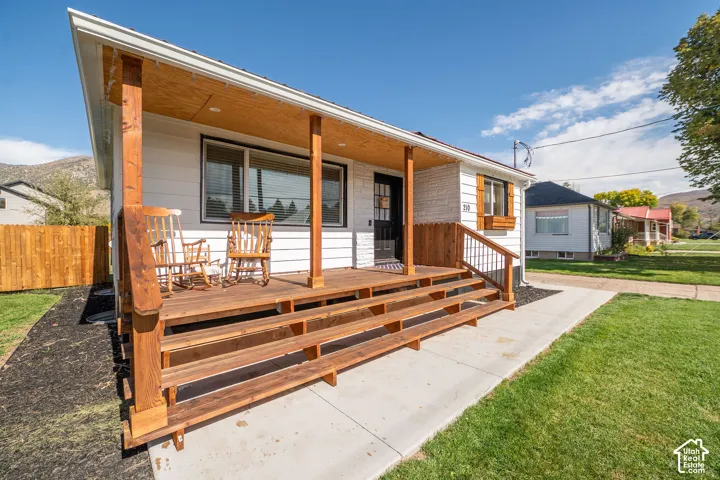 Front exterior featuring white siding, a wood-finish porch with railings, multiple steps, and a concrete walkway
