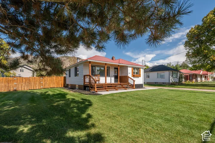 White exterior with a red roof, a wooden porch, and a well-maintained lawn