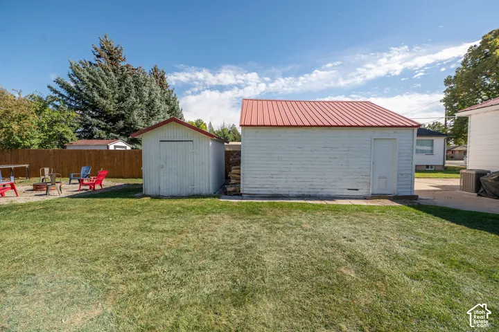 Expansive grass lawn with two outbuildings, a wood fence, and mature trees