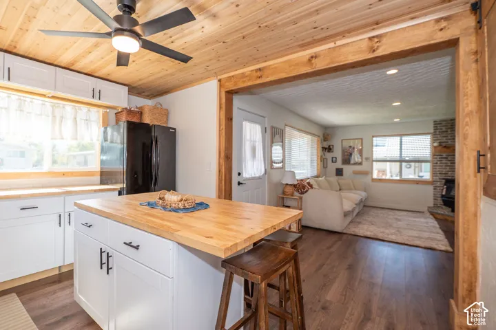 Kitchen with wood-finish ceiling, white cabinetry, a center island with a wood countertop, and a black refrigerator