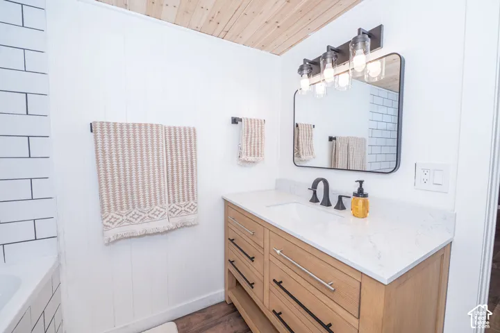 Wood-paneled ceiling, white subway tile, wood-finish vanity with drawer storage, white countertop, and matte black fixtures