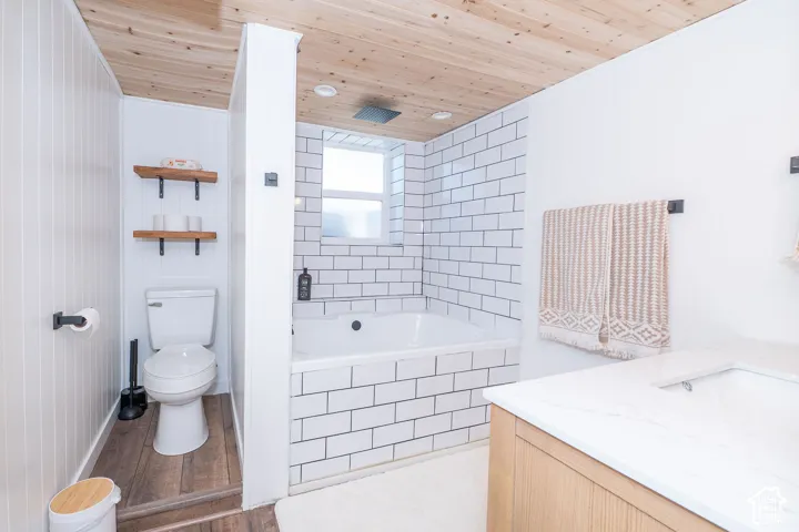 Wood-finish plank flooring, wood plank ceiling, subway tile bath surround, built-in bathtub, and a wood-finish vanity with a white countertop