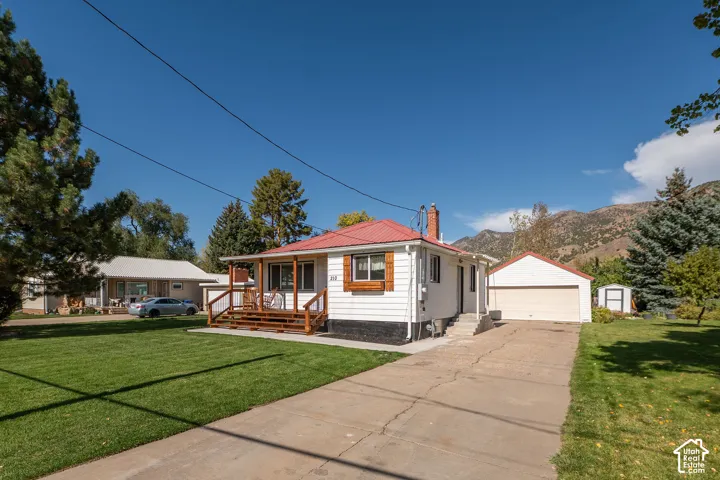 White exterior with red roof, front porch with wood railing, attached garage, concrete driveway, and a manicured lawn
