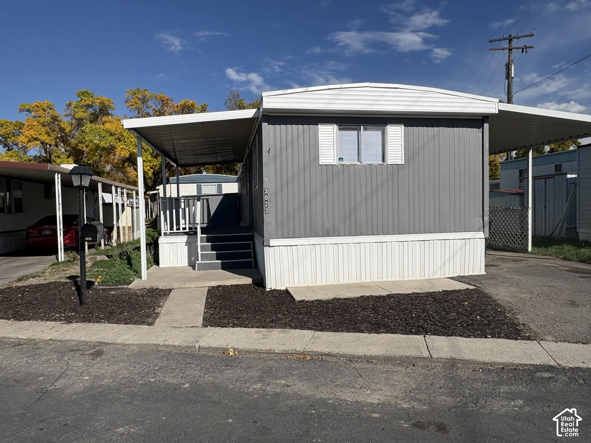 Grey exterior siding with white trim, covered porch with steps, covered carport, and paved driveway