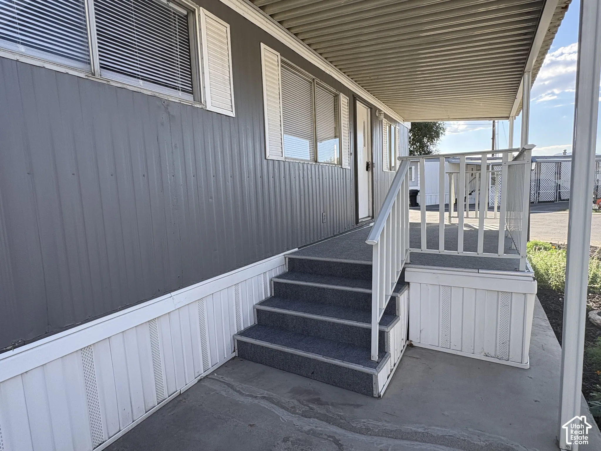 Covered porch entry featuring a white railing and gray carpeting