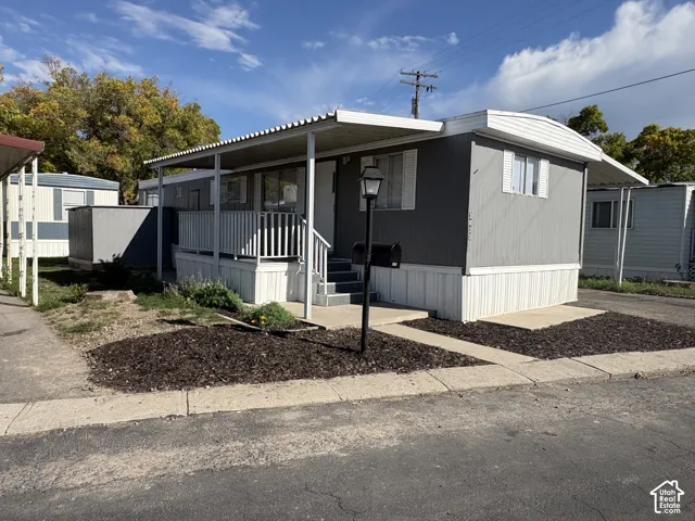 Covered front porch, gray siding, white skirting, paved walkway, and a mail post with a lamp