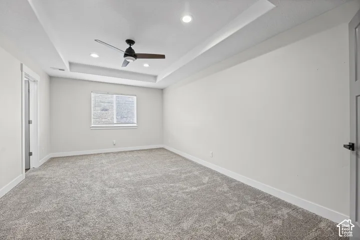 Recessed tray ceiling, integrated ceiling fan, recessed lighting, wall-to-wall carpeting, and a window with blinds