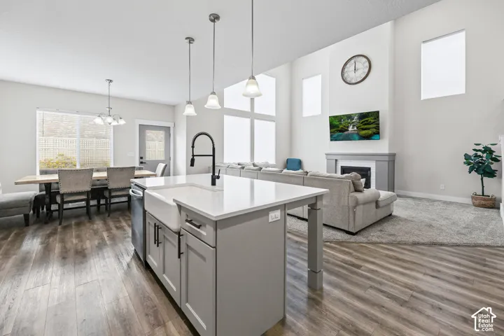 Open-concept living space featuring wood-finish flooring, a kitchen island with pendant lighting, and a fireplace with a mantel
