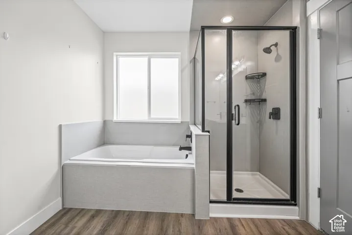 Soaking tub with a privacy window, walk-in shower with black-framed glass enclosure, and wood-finish flooring