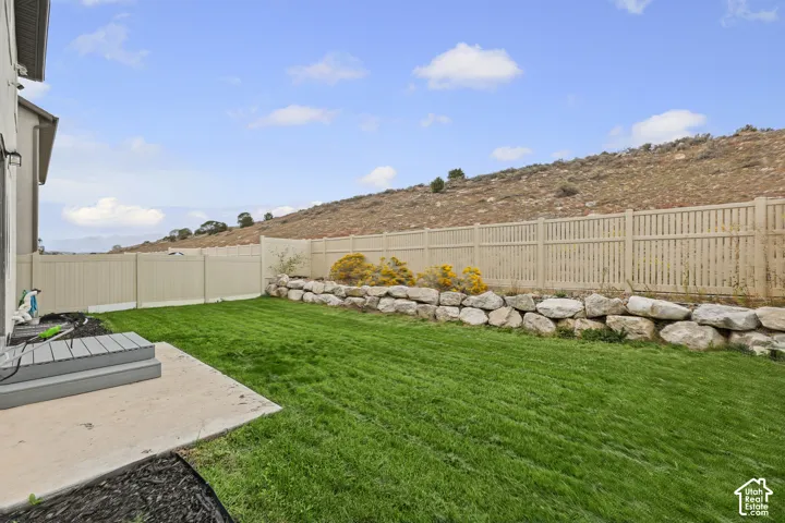 Expansive backyard featuring a green lawn, concrete patio, and a stone retaining wall