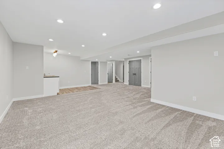Expansive carpeted area with recessed lighting, light gray wall finishes, and white trim