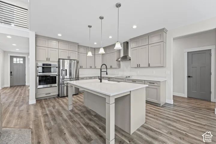 Kitchen featuring wood-finish flooring, light grey cabinetry, white countertops, stainless steel appliances, and a center island with a black faucet