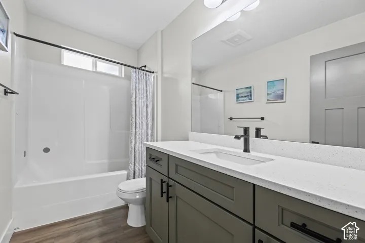 Bathroom featuring wood-finish flooring, a white integrated tub and shower unit, a vanity with a white countertop, a black faucet, and a large mirror