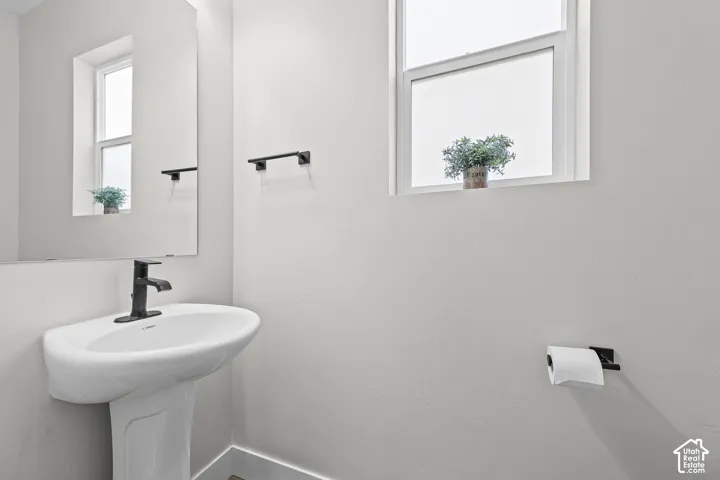 Pedestal sink with a matte black faucet, wall-mounted mirror, and a single window