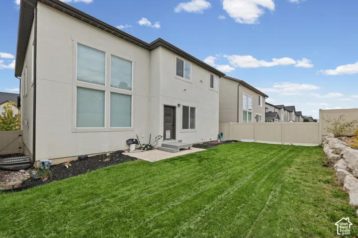 Expansive green lawn, stucco exterior, multiple large windows, rear entry door with steps, and a privacy fence