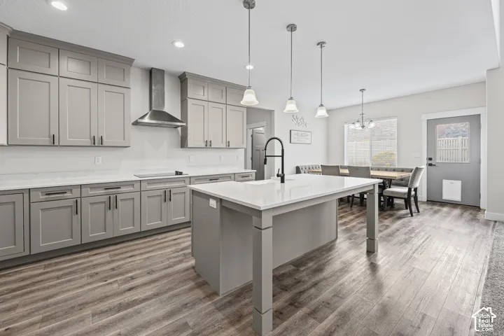 Kitchen featuring grey shaker-style cabinetry, white countertops, stainless steel range hood, central island with a black faucet, and wood-finish flooring