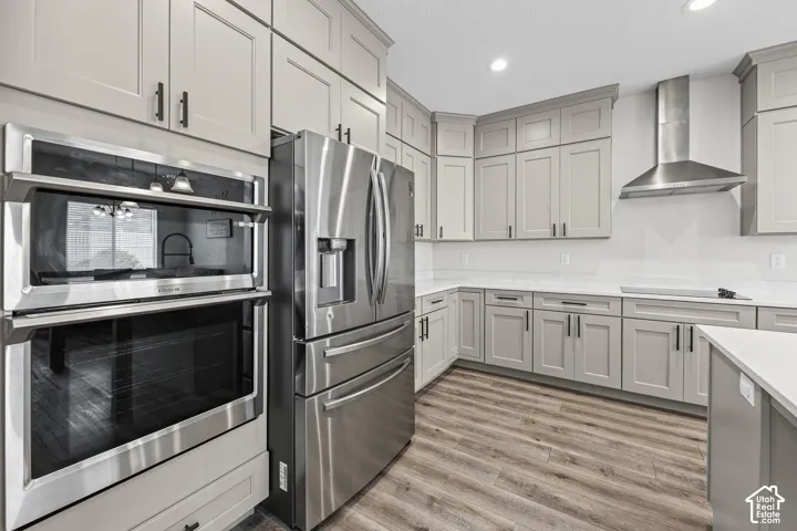 Stainless steel appliance suite, light-toned cabinetry, wood-finish flooring, white countertops, and a modern range hood