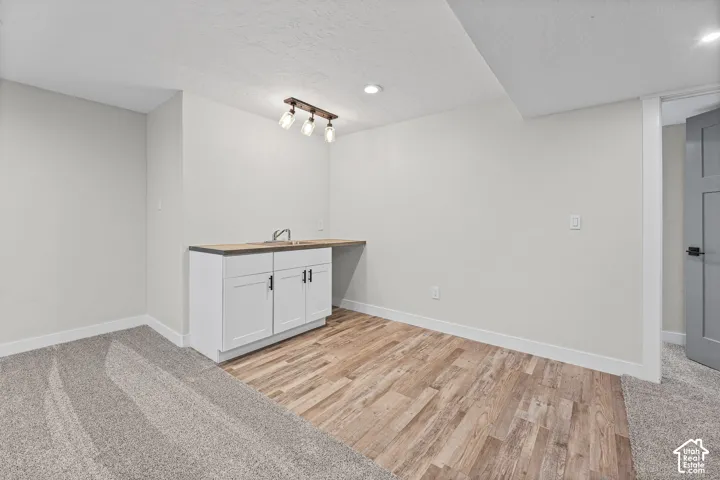 White cabinetry with black hardware, wood-finish countertop, stainless steel sink, and track lighting fixture