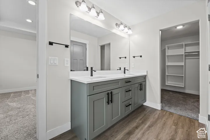 Dual vanity with a white countertop and undermount sinks, wood-finish flooring, and sconce lighting