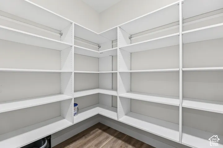Spacious pantry featuring extensive built-in white shelving and wood-finish flooring