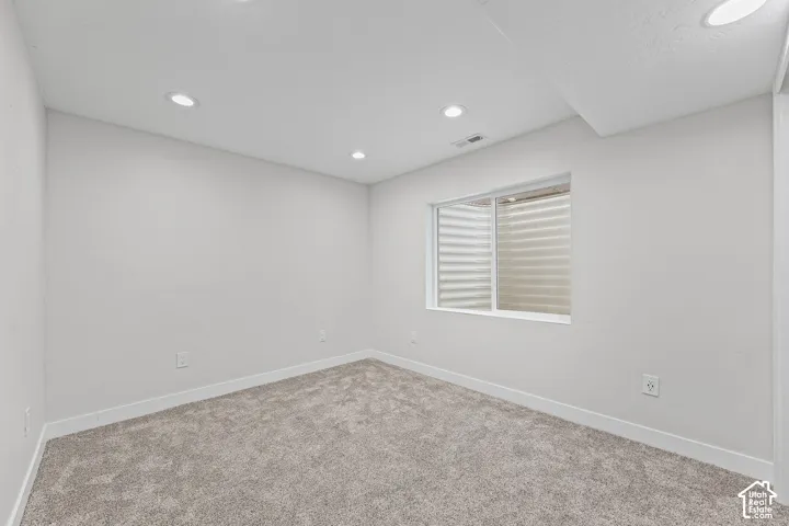 Recessed ceiling lighting, light gray wall paint, white trim, carpet flooring, and a single window