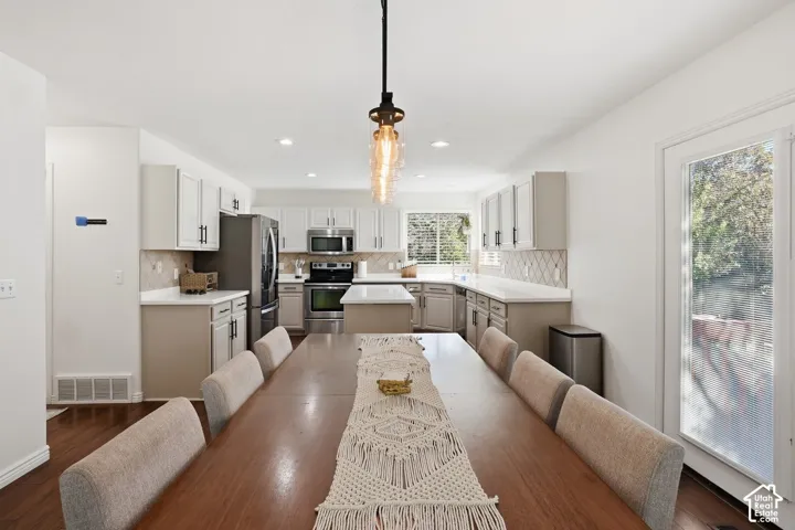 Kitchen featuring stainless steel appliances, white cabinetry, light-toned countertops, tile backsplash, and wood-finish flooring