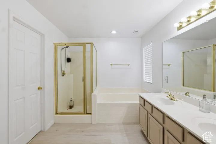 Bathroom featuring a dual vanity with a light countertop, gold-finish hardware, a built-in tub, and a glass-enclosed shower