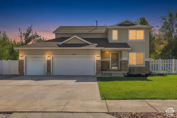 Stucco exterior with stone accents, attached two-car garage, concrete driveway, and front lawn
