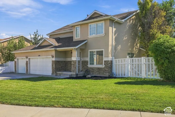 Two-story residence featuring a stucco and stone veneer exterior, a two-car garage, and a white picket fence