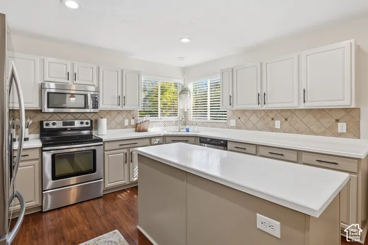 Recessed lighting, wood-finish flooring, two-tone cabinetry with black hardware, stainless steel appliances, and a central island with a white countertop