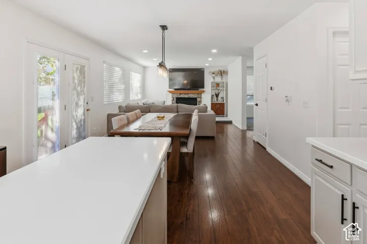 Wood-finish flooring throughout, white shaker-style cabinetry with matte black hardware, white countertops, recessed lighting, and a stone-clad fireplace
