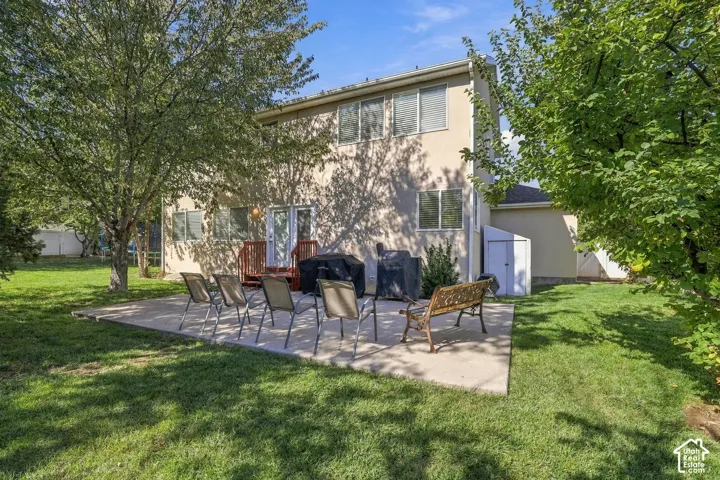 Expansive backyard featuring a concrete patio, mature trees, and a wooden deck with railing