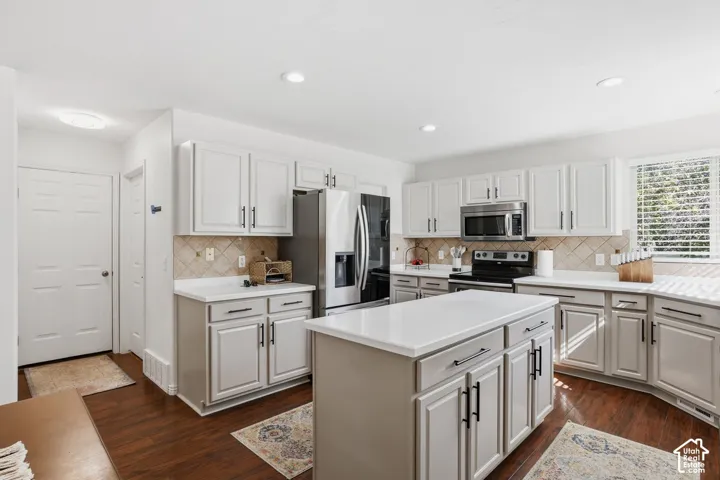 Kitchen featuring white cabinetry, stainless steel appliances, a center island with countertop, tile backsplash, and wood-finish flooring
