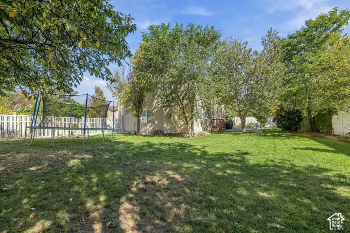 Expansive backyard featuring a manicured lawn, mature trees, and a white picket fence