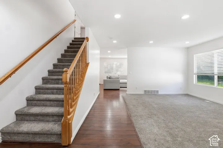 Carpeted staircase with wood banister, recessed lighting, wood-finish flooring, and large windows with blinds
