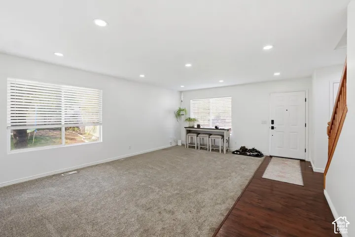Recessed ceiling lighting, wood-finish flooring, two windows with blinds, and a built-in staircase with wood railing