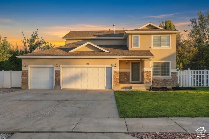 Stucco exterior with stone accents, a three-car garage, white picket fencing, and a manicured lawn