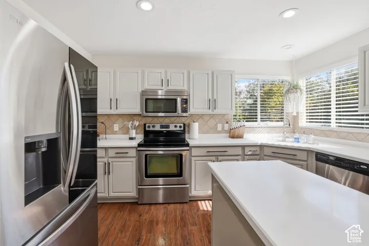Kitchen featuring stainless steel appliances, white cabinetry, a white countertop island, wood-finish flooring, and a tiled backsplash