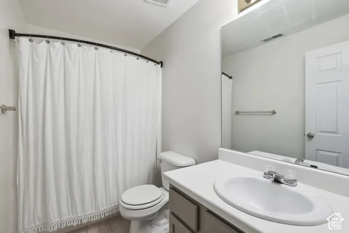 Bathroom featuring a single vanity with a white countertop and integrated sink, a large wall-mounted mirror, and a curved shower rod