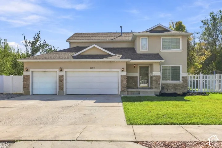 Stucco exterior with stone accents, two-car garage, concrete driveway, front lawn, and white picket fencing