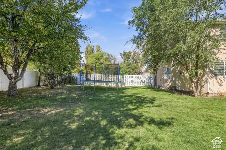 Expansive backyard featuring a green lawn, mature trees, and white privacy fencing