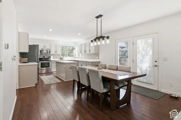 Hardwood-finish flooring throughout, kitchen with stainless steel appliances, white cabinetry, island with countertop seating, and a geometric tile backsplash