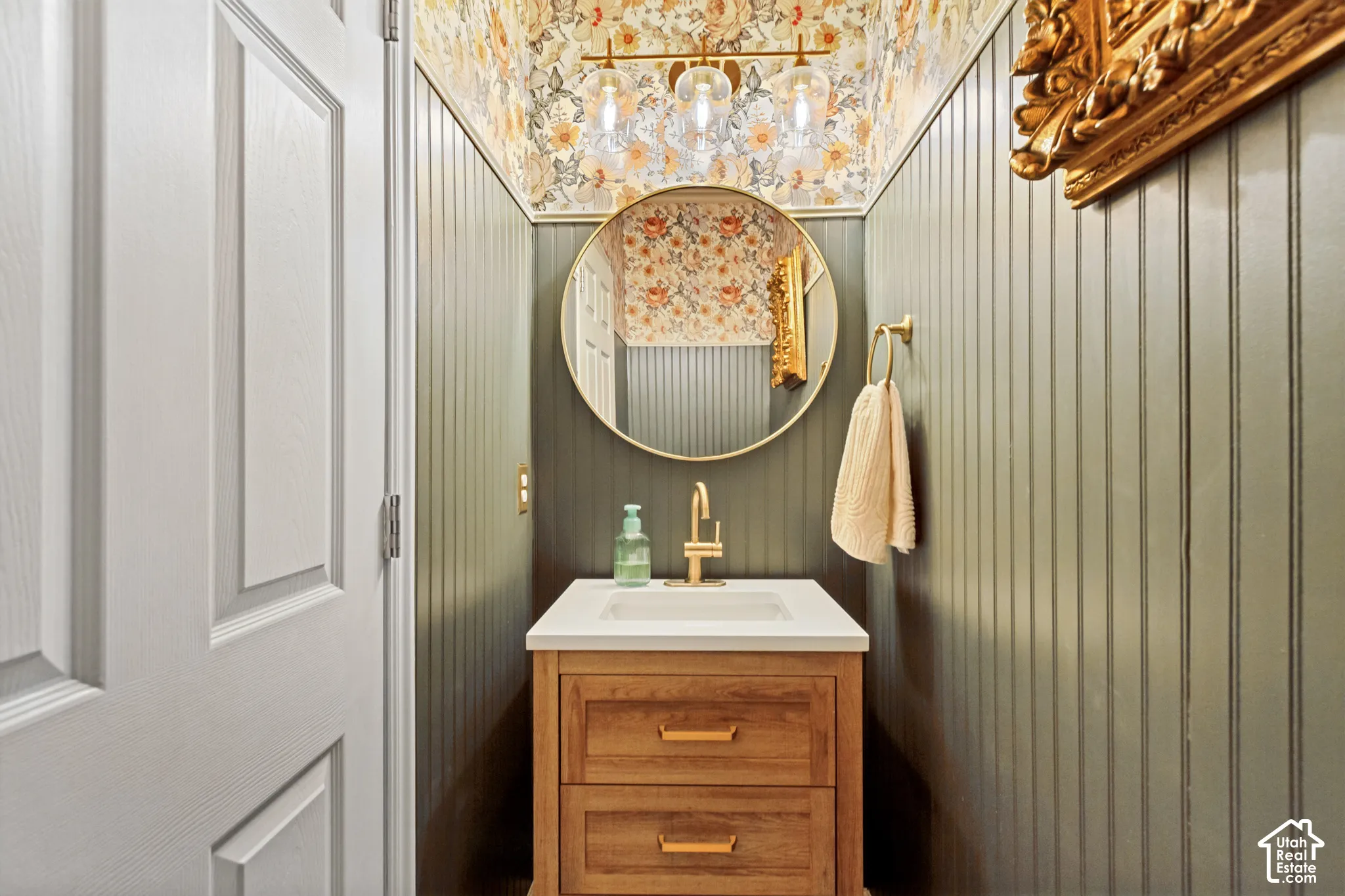 Vanity with wood-finish cabinetry, white countertop, and gold-tone faucet